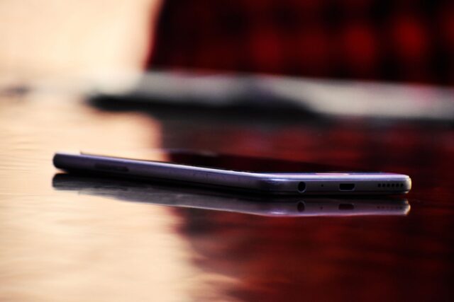 Telefon așezat cu ecranul în jos pe o masă de lemn, lângă o ceașcă de ceai și o carte deschisă